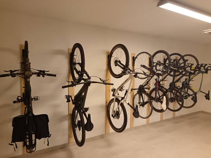 Bicicletas colgadas en soportes de pared en un garaje o trastero, con una bicicleta a la izquierda y varias a la derecha.