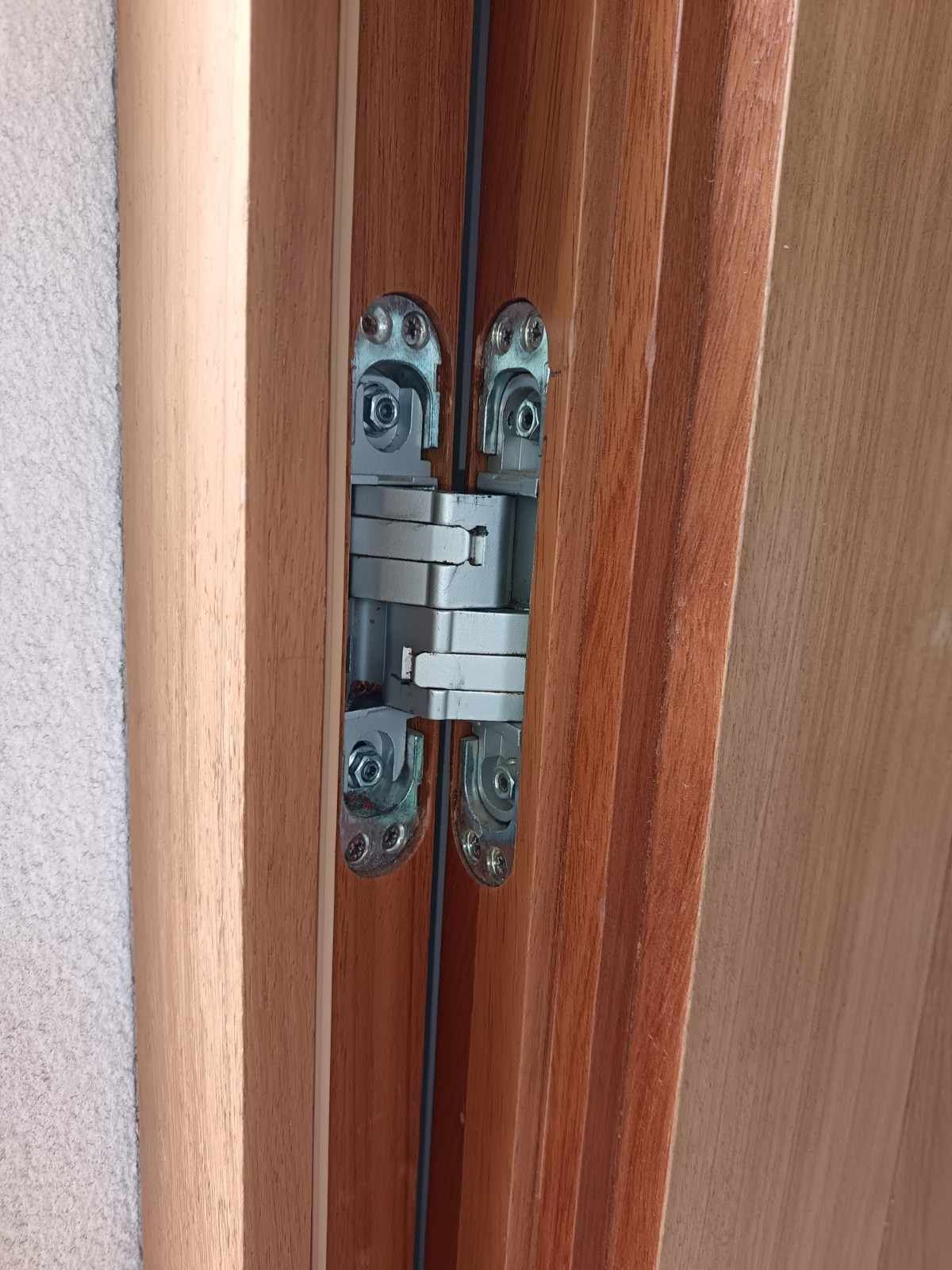Primer plano de una bisagra de puerta plateada entre dos paneles de puerta de madera.