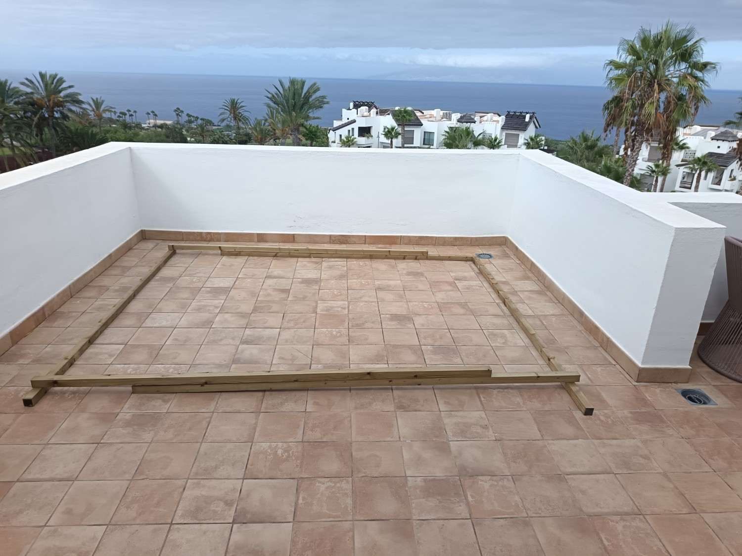 Terraza en la azotea con azulejos, paredes blancas y vistas al océano a lo lejos.