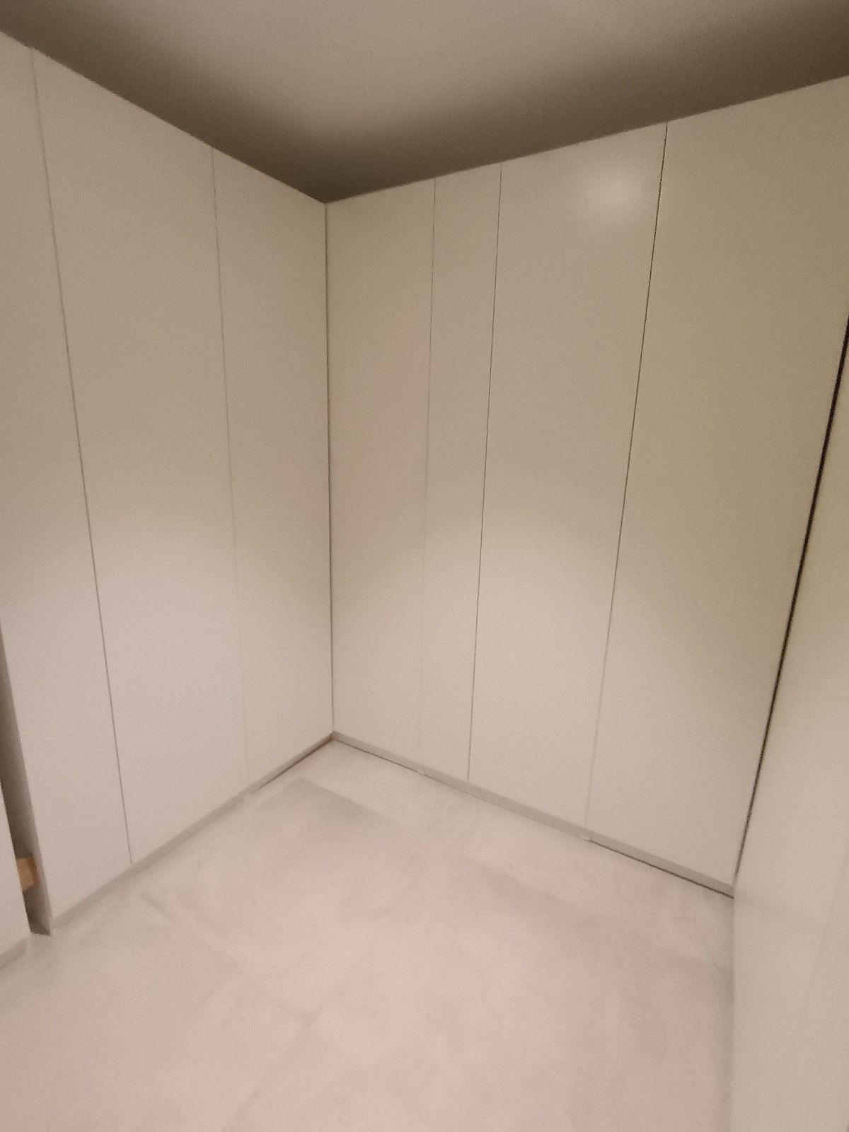 Habitación esquinera blanca y vacía con armarios empotrados y suelo claro.
