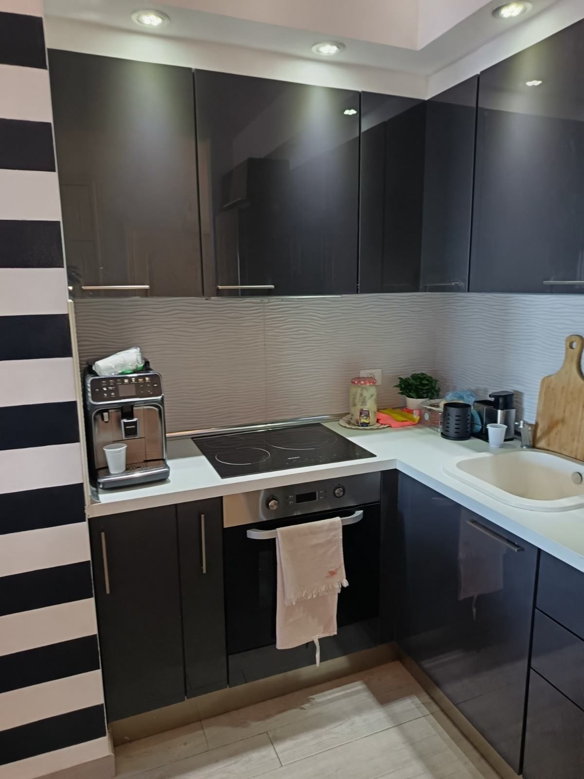 Cocina moderna en blanco y negro con armarios, encimera, estufa, fregadero y cafetera.