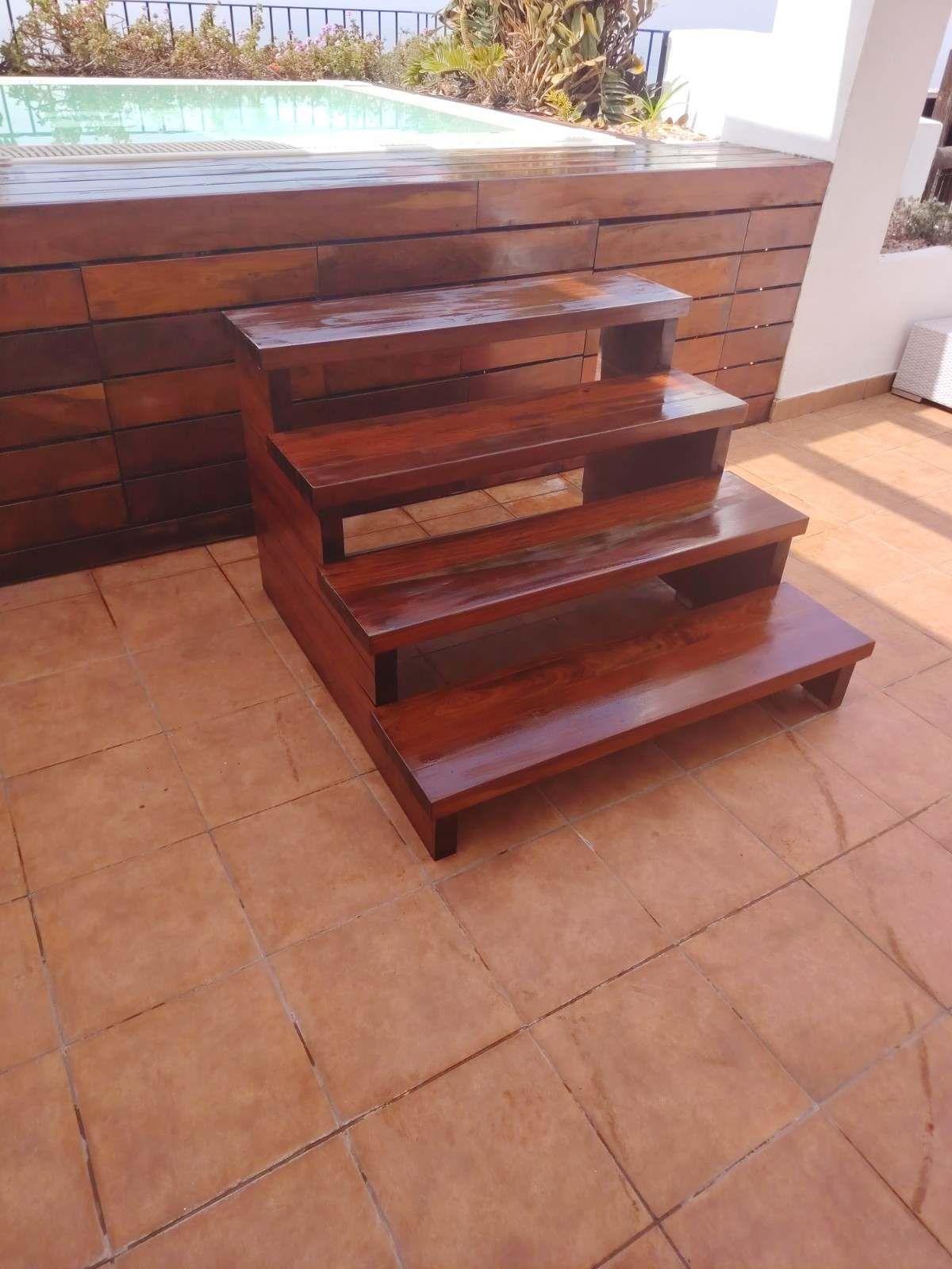 Escaleras de madera que conducen a una bañera de hidromasaje elevada en un patio embaldosado.