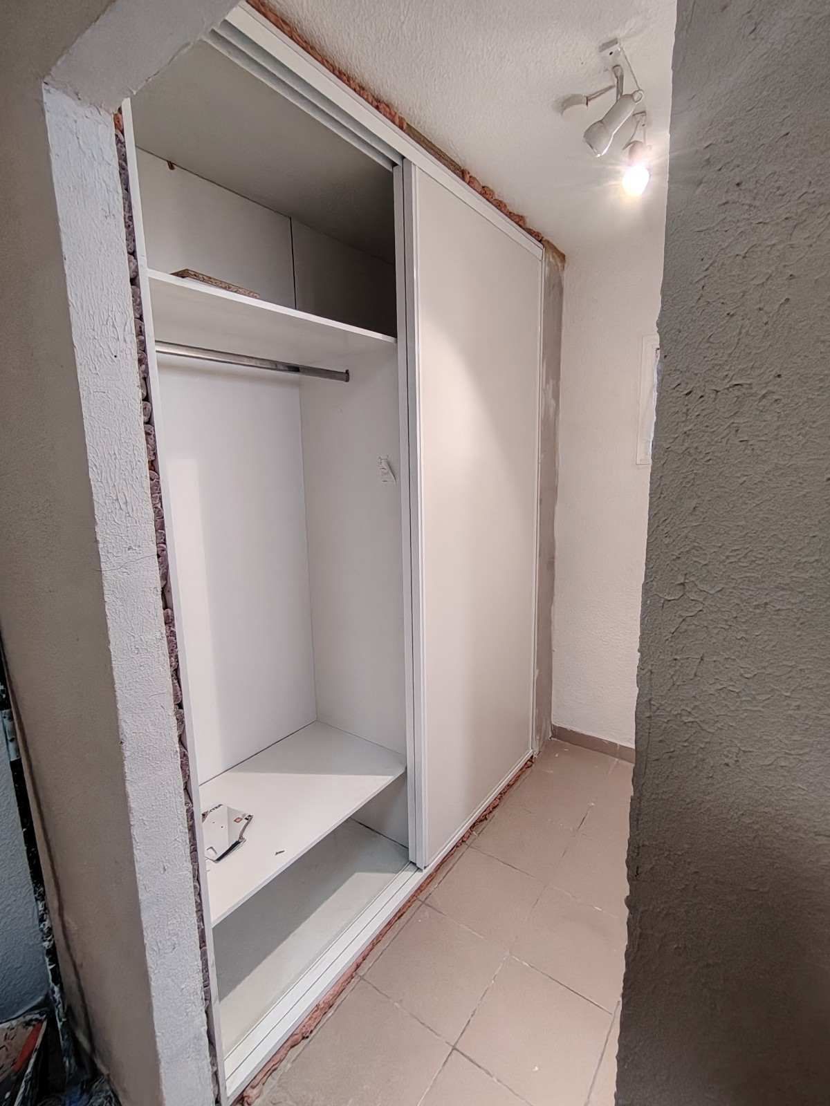 Armario empotrado abierto con estantes y barra para colgar ropa en una habitación alicatada.