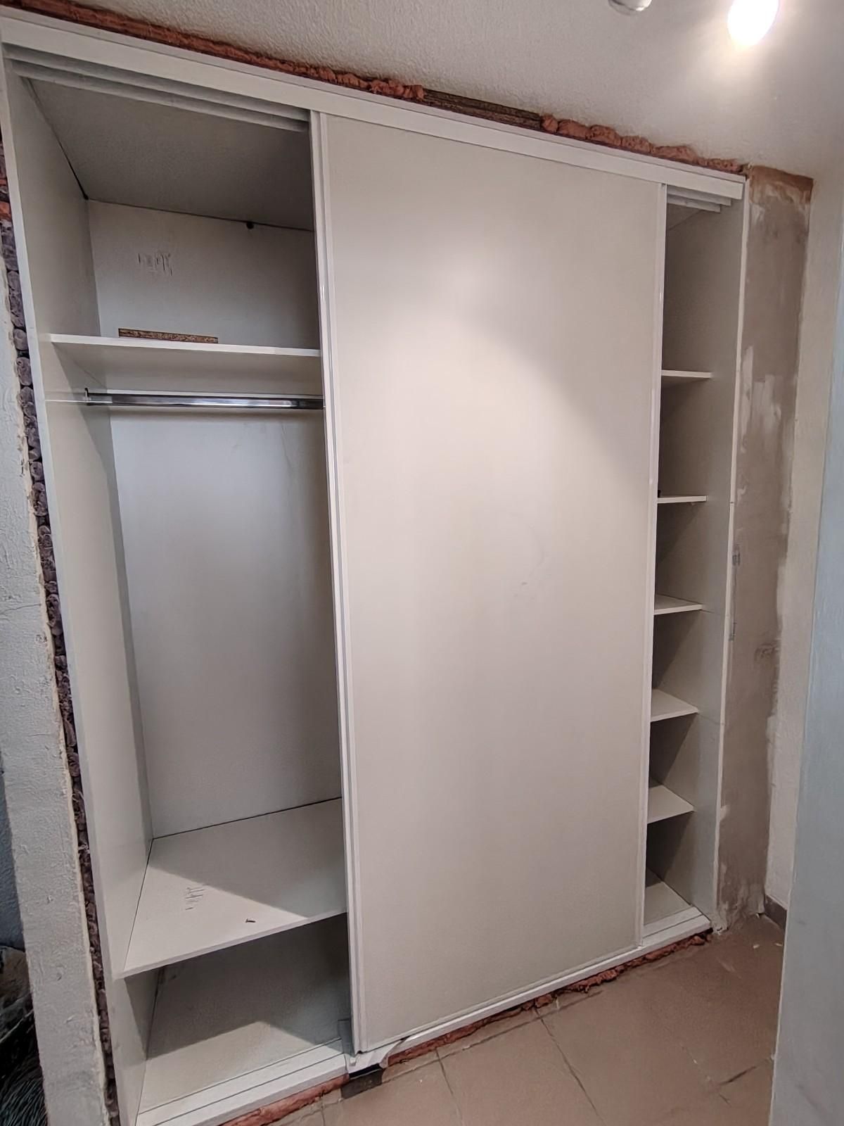 Armario blanco con puertas correderas y estantes abiertos parcialmente ensamblado en una habitación.