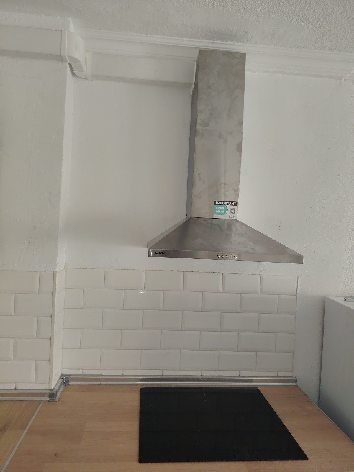 Pequeña zona de cocina con campana extractora de acero inoxidable sobre una alfombra negra y un salpicadero de azulejos blancos.