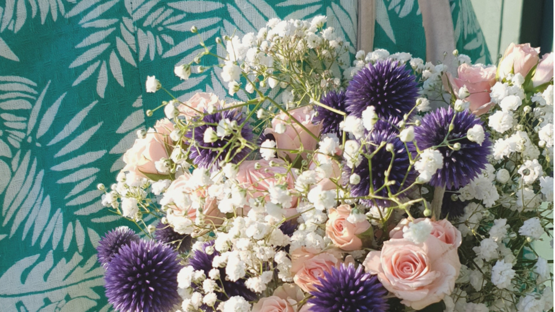 Bouquet de roses pastel, de fleurs blanches et de chardons violets sur un fond de feuillage turquoise