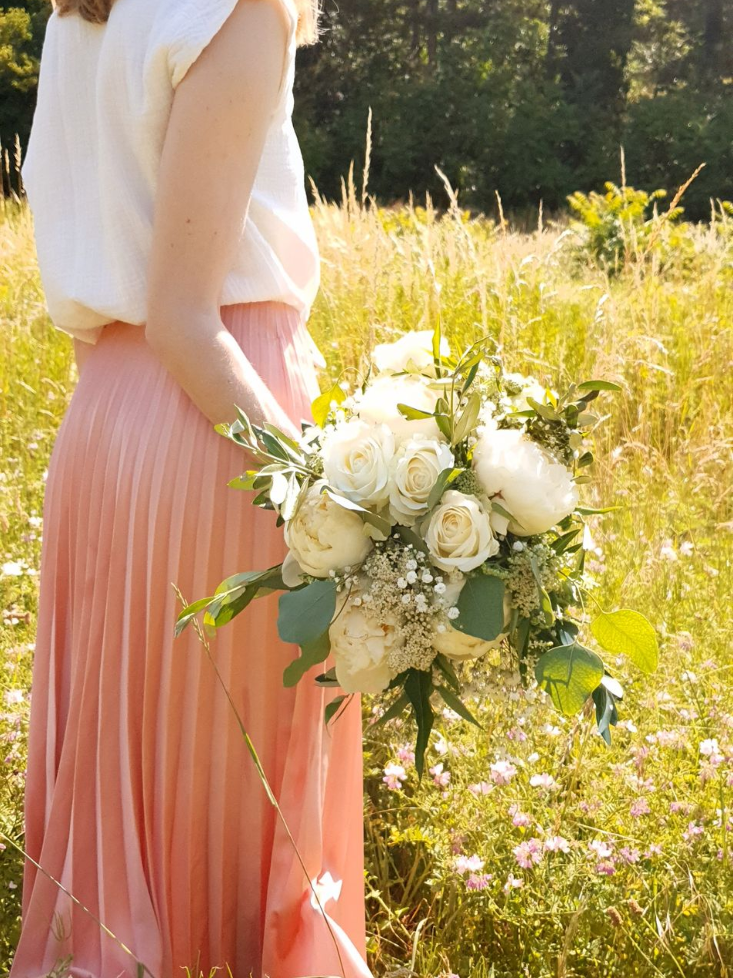 Une personne en jupe rose tenant un bouquet de fleurs blanches dans une prairie ensoleillée