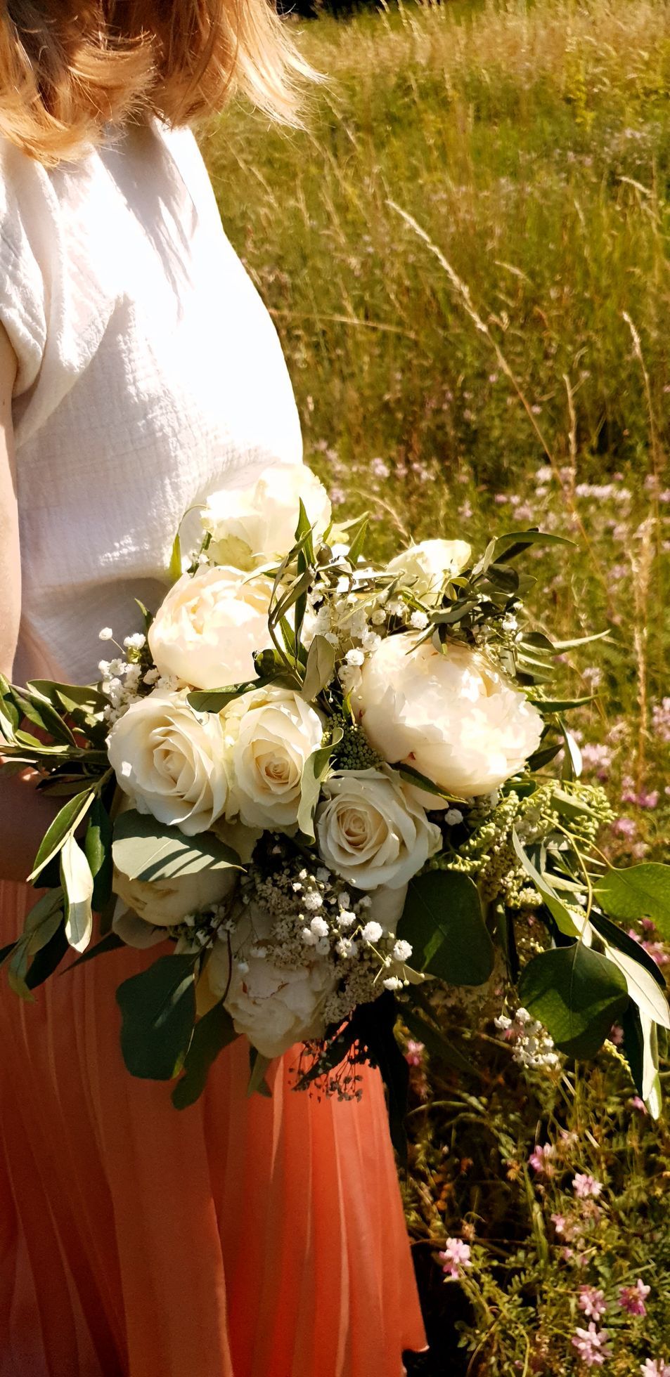 Une personne tenant un bouquet de roses blanches et de verdure dans un champ ensoleillé