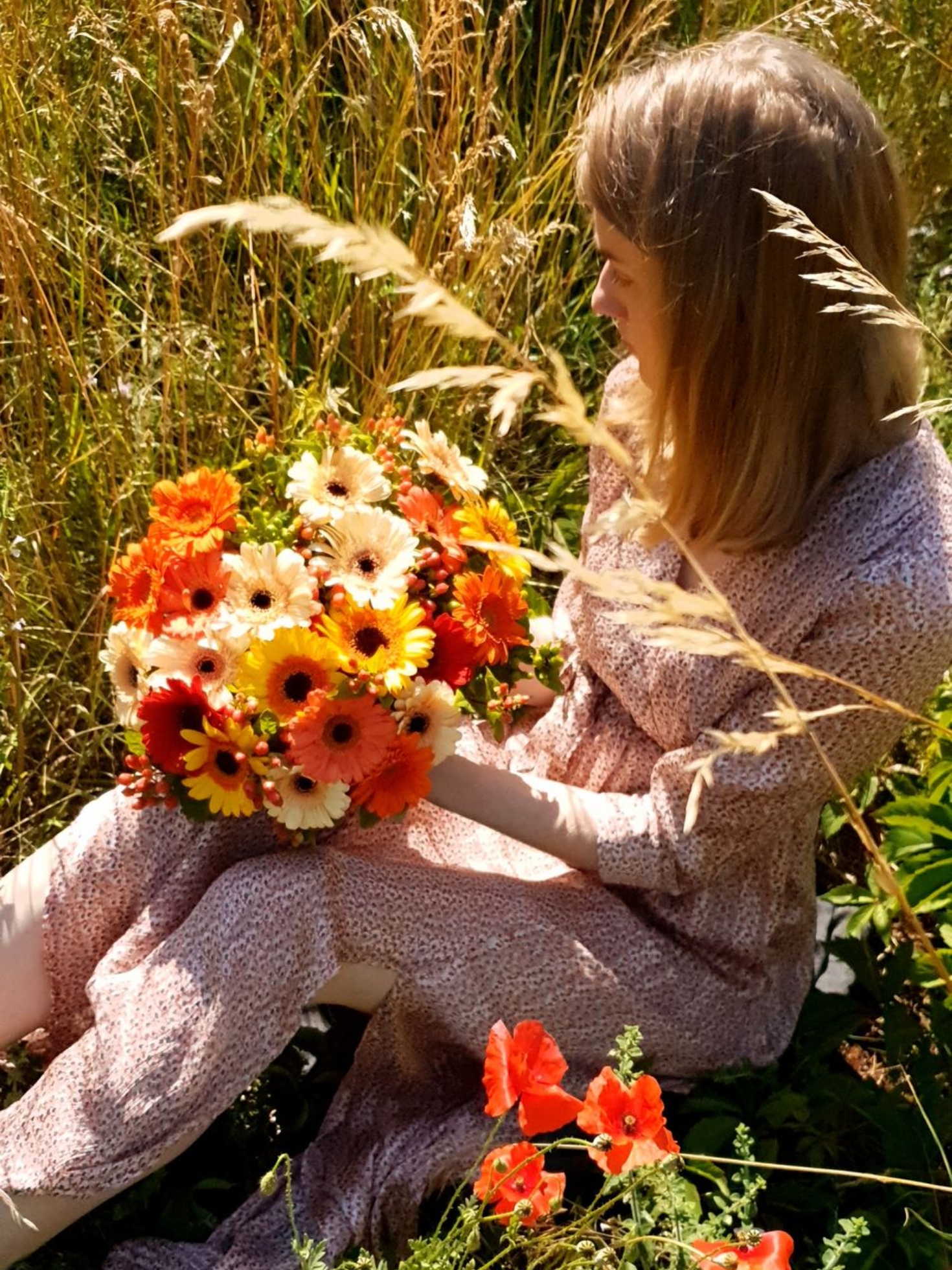 Une personne assise dans les hautes herbes tient un bouquet de fleurs orange et blanches.