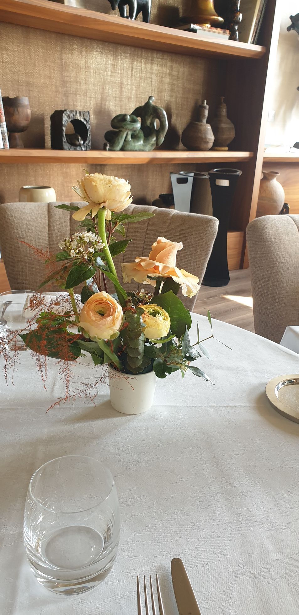 Composition florale sur une table blanche dans une pièce chaleureuse avec des étagères et des éléments de décoration en arrière-plan