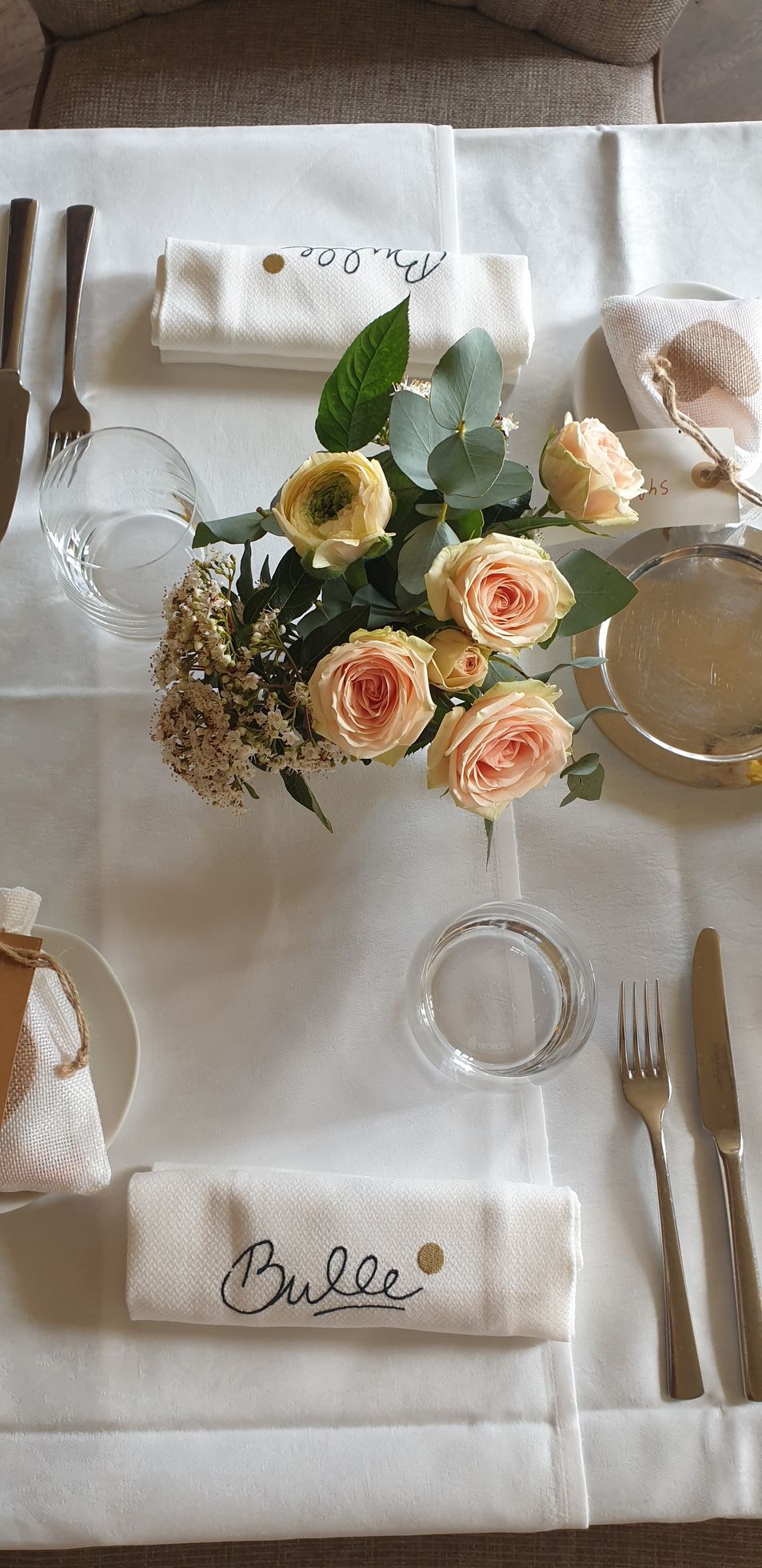 Élégante table dressée avec serviette blanche, roses couleur pêche, verdure et ustensiles dorés