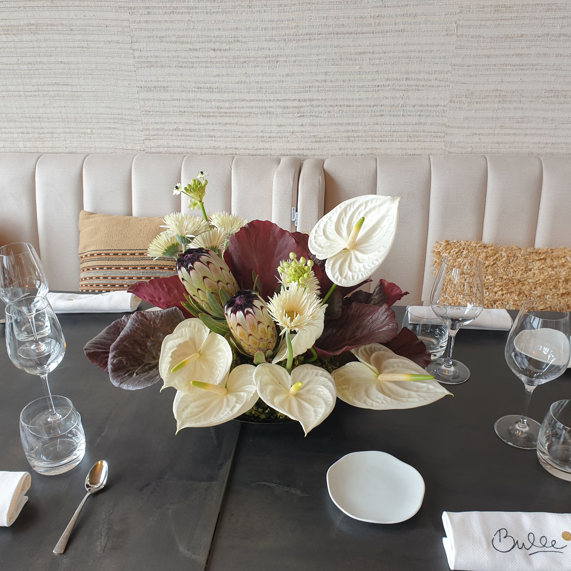 Centre de table floral sur une table à manger dressée avec verres à vin, chaises blanches et décoration beige