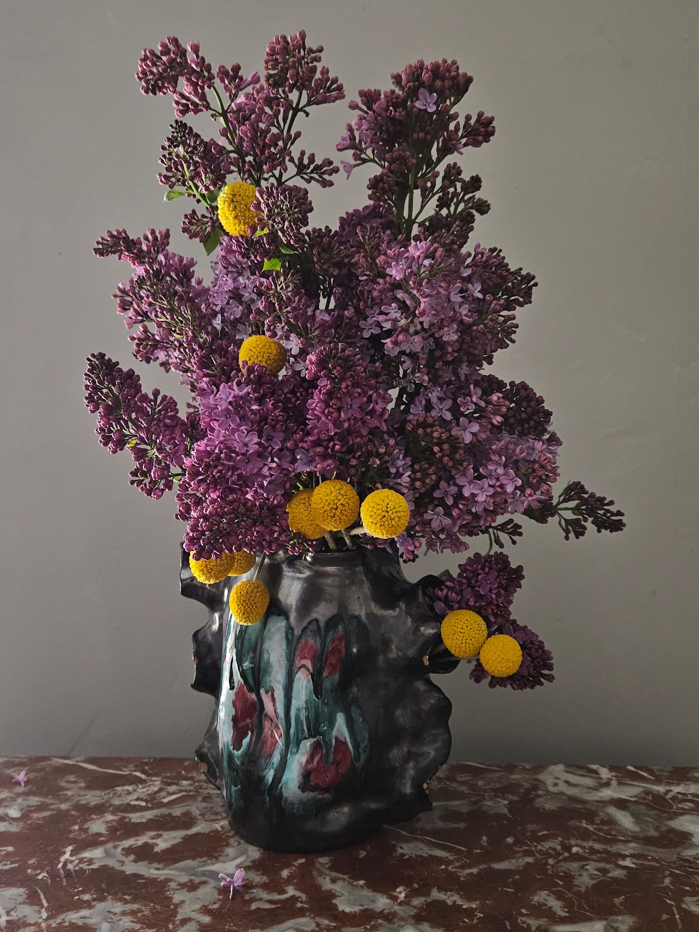 Fleurs violettes à pétales jaunes dans un vase décoratif en céramique, sur une table à motifs.