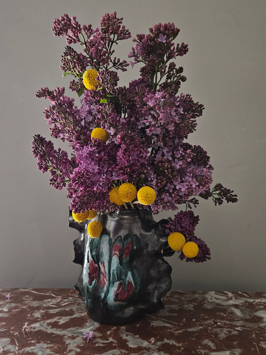 Fleurs violettes à pétales jaunes dans un vase décoratif sombre, sur une table à motifs.