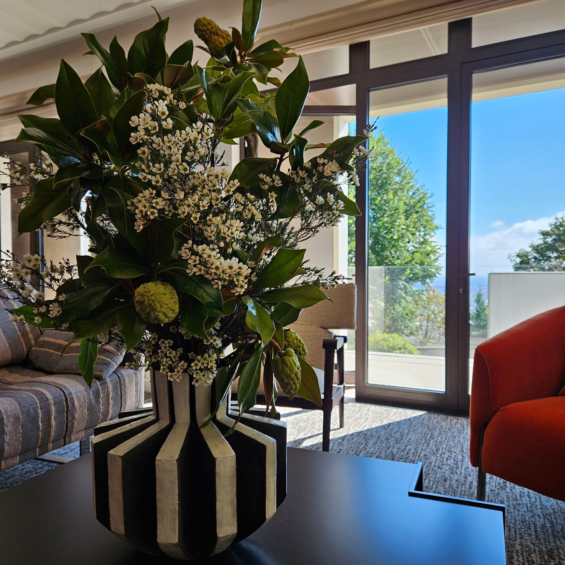 Vase de fleurs en noir et blanc sur une table dans un salon lumineux, près de grandes fenêtres