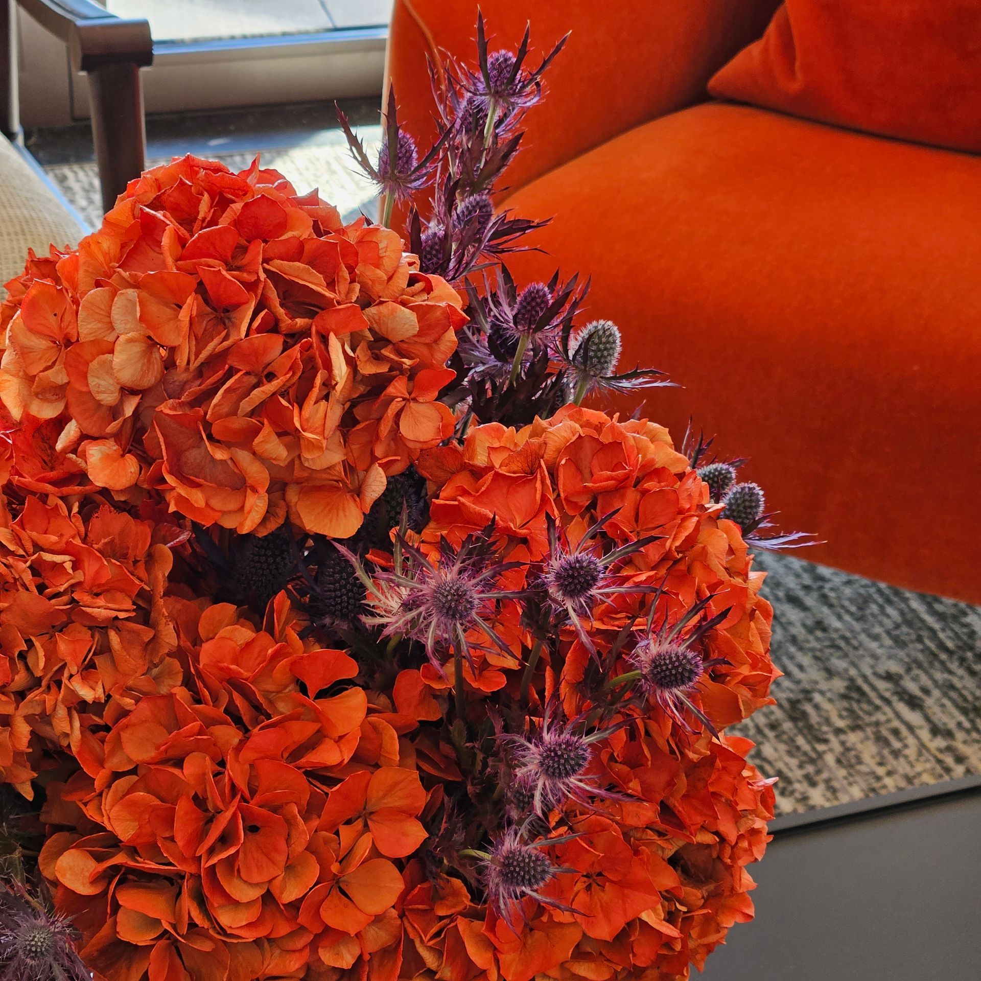 Des fleurs orange et violettes dans un vase sur une table à côté d'un canapé orange