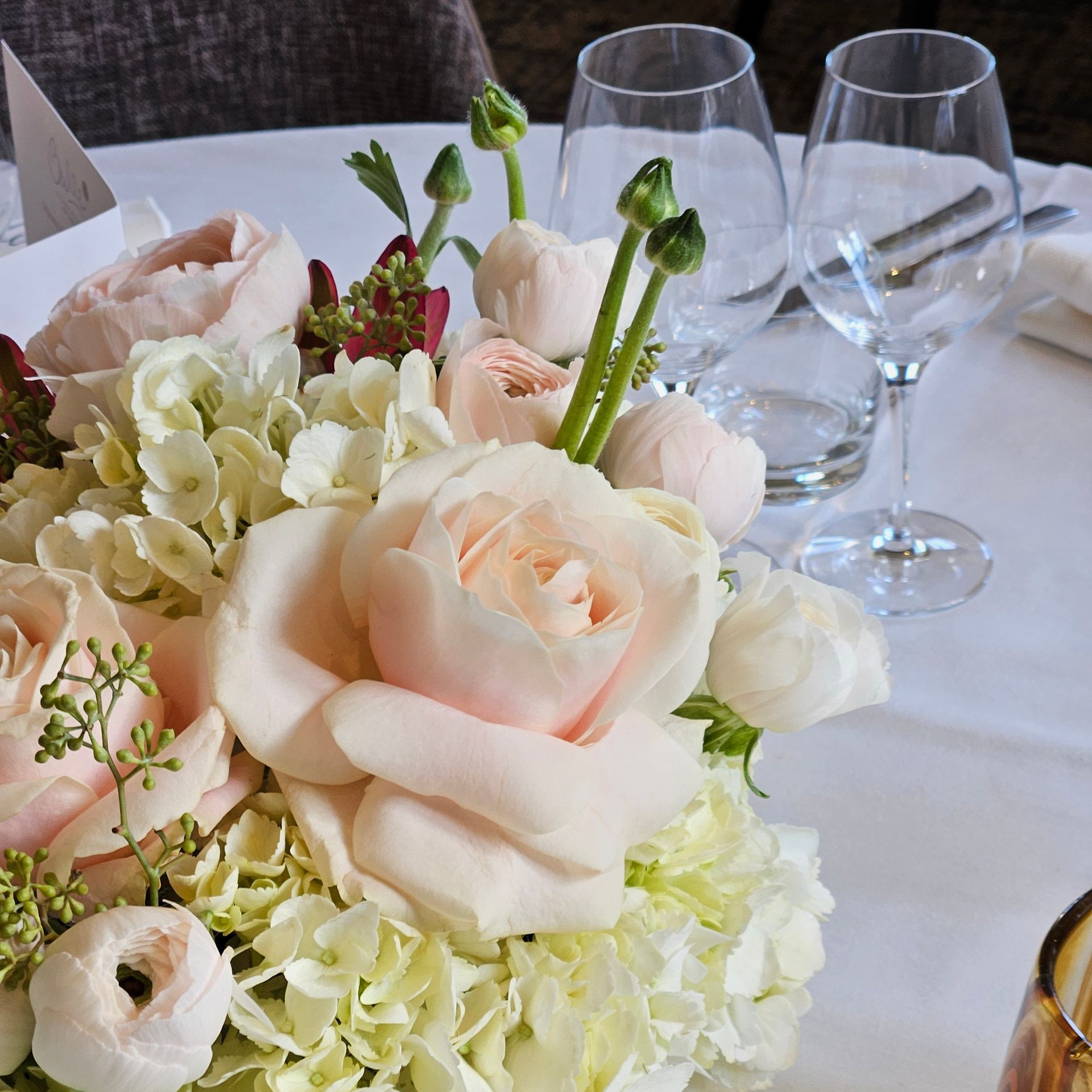 Centre de table floral pastel composé de roses et d'hortensias sur une table blanche dressée avec des verres à vin.