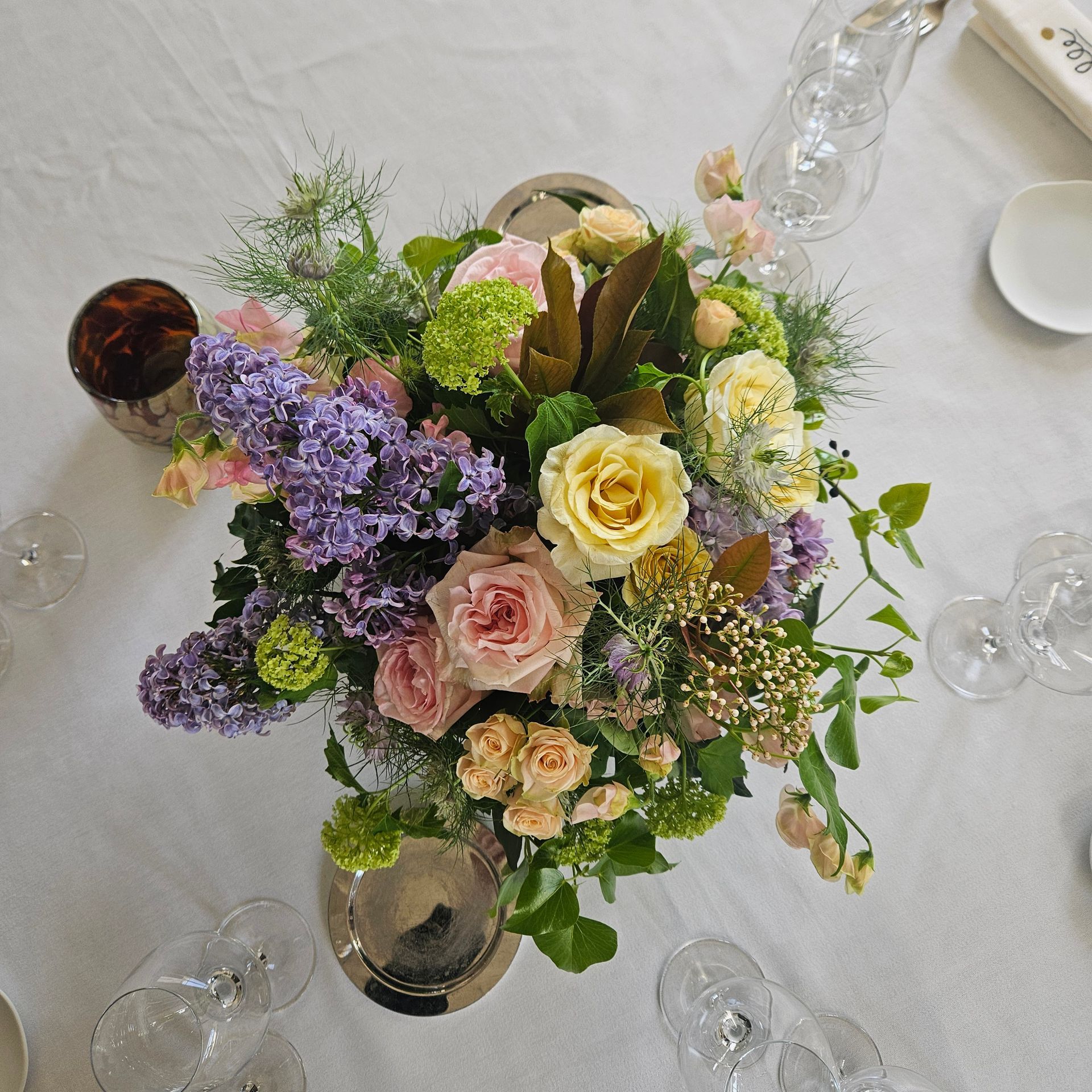 Vue de dessus d'un arrangement floral pastel composé de roses et de lilas sur une table blanche avec des verres