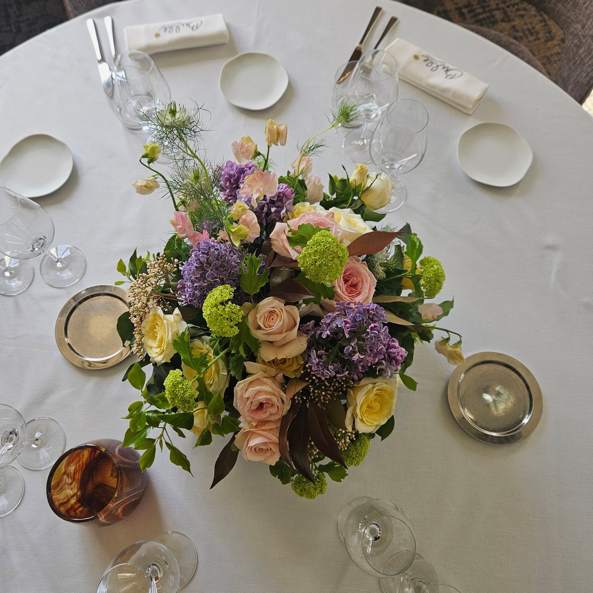 Table de banquet ronde avec un centre de table floral aux tons pastel, couverts blancs et verrerie.