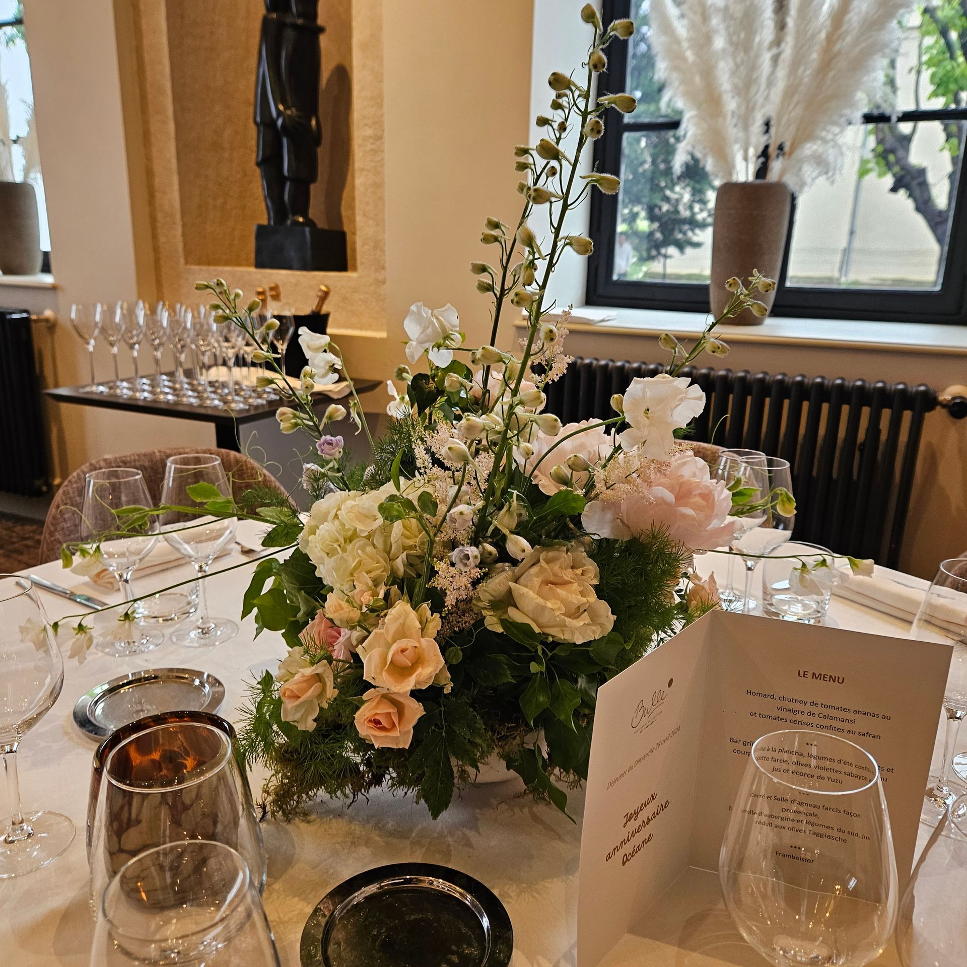 Élégante table de banquet avec un centre de table floral blanc et crème, de la verrerie et des marque-places pliés près d'une fenêtre