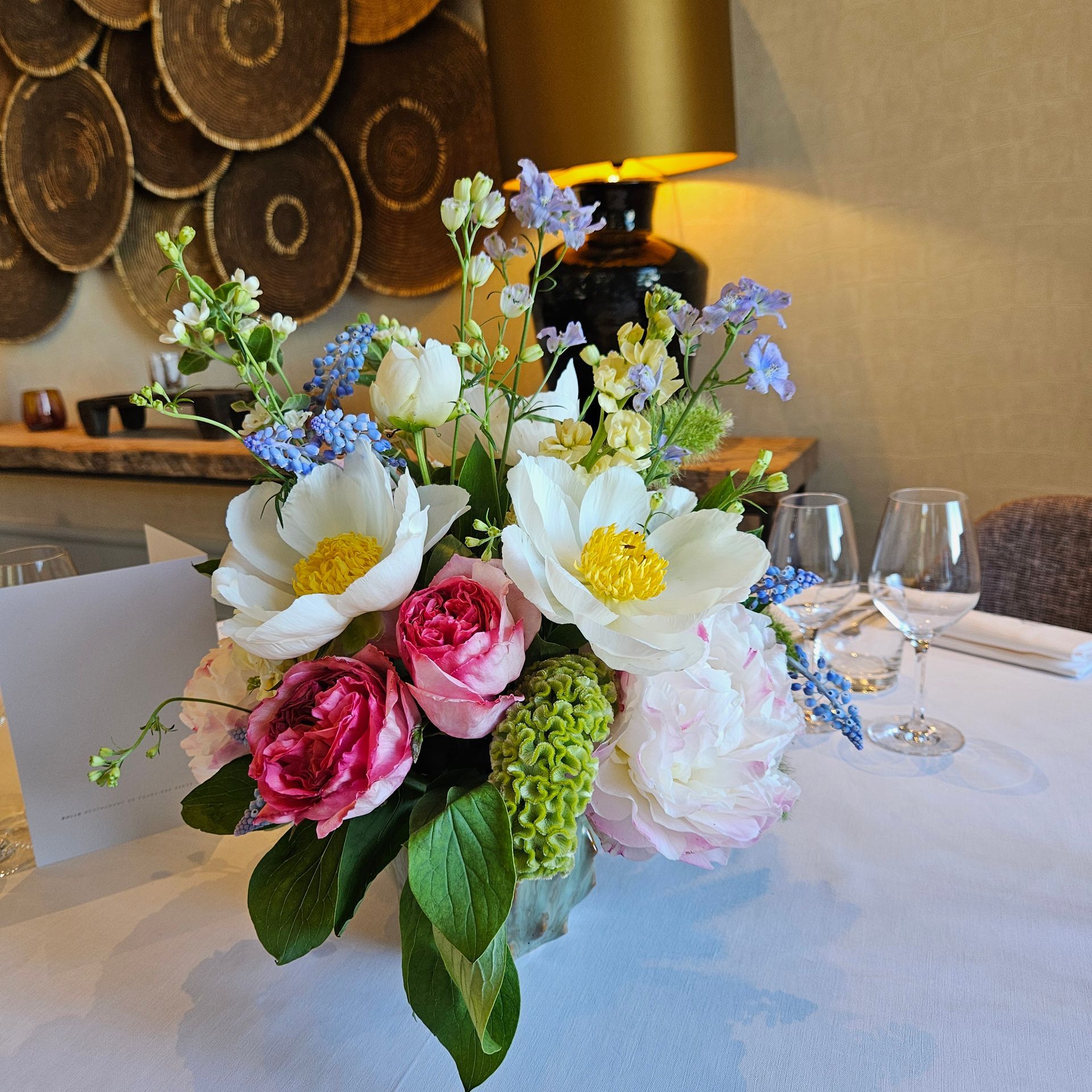 Centre de table floral composé de fleurs blanches, roses et bleues sur une table dressée dans un restaurant