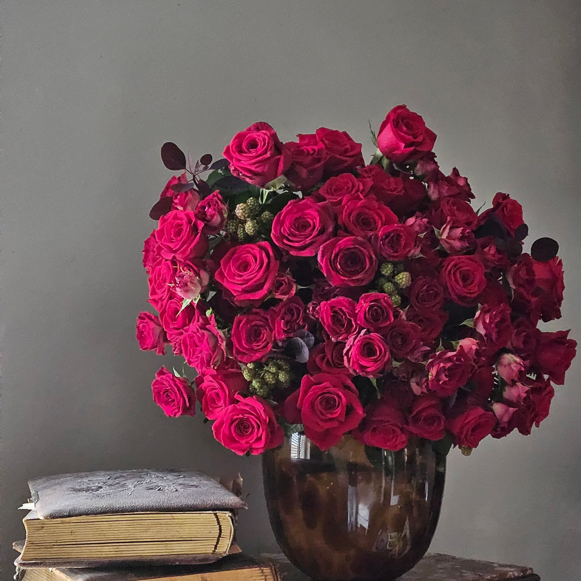 Bouquet de roses rose foncé dans un vase marron à côté de livres empilés sur une surface grise