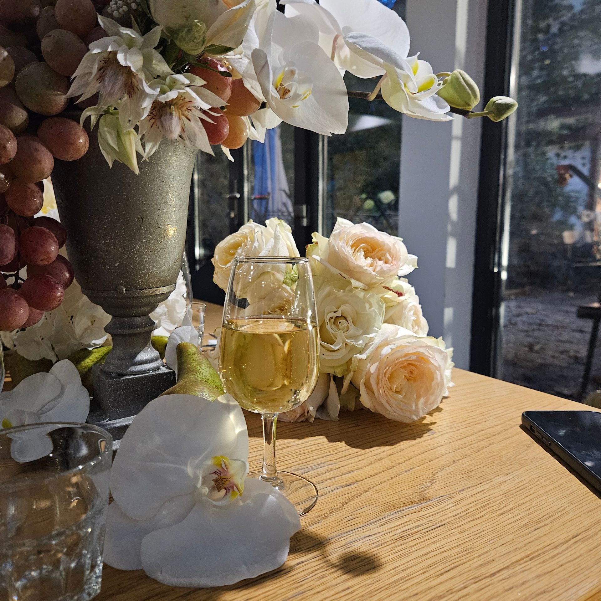 Des fleurs blanches et un verre de vin sur une table ensoleillée près d'une fenêtre