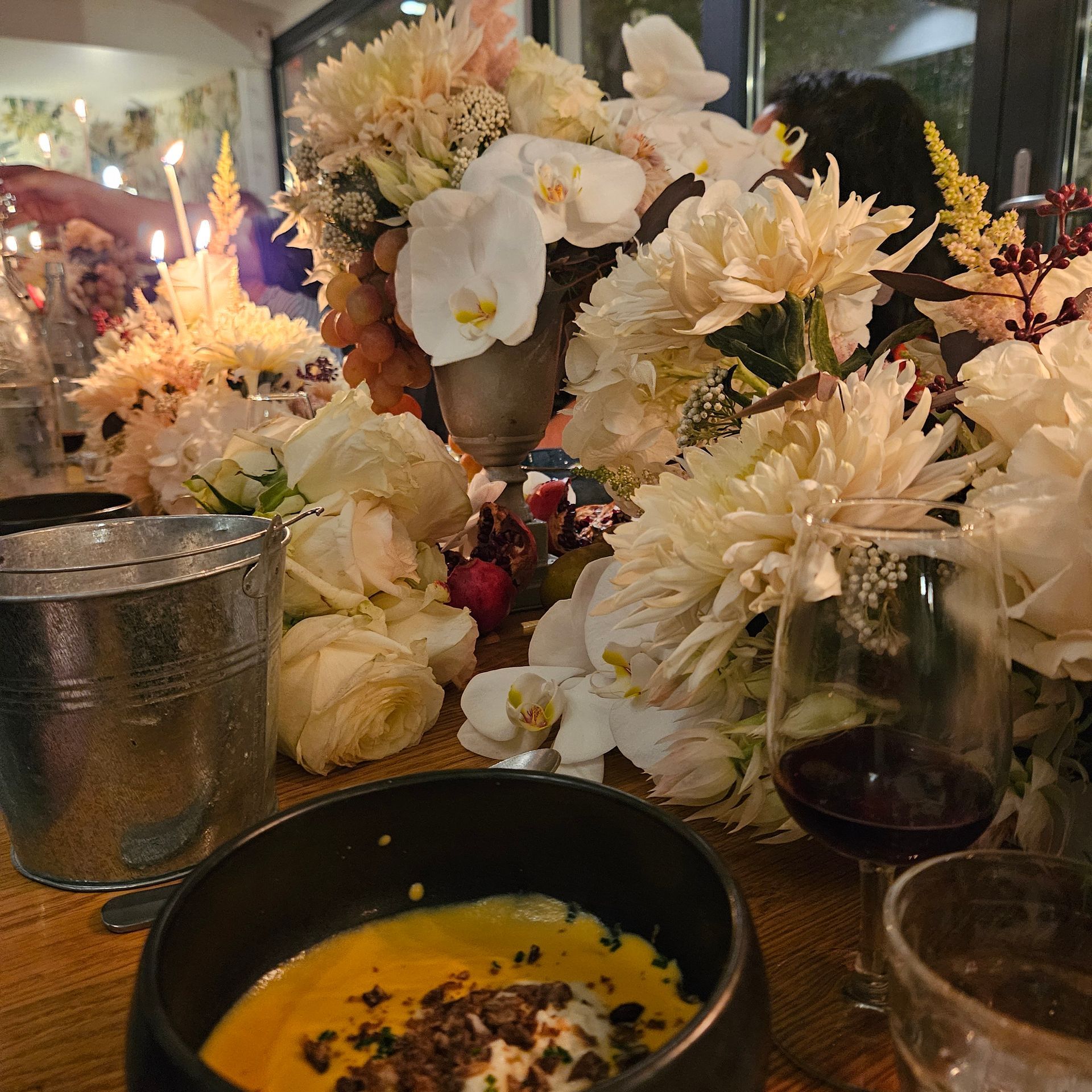 Centre de table floral composé de fleurs blanches et crème sur une table de restaurant éclairée aux chandelles, avec bols et verres.