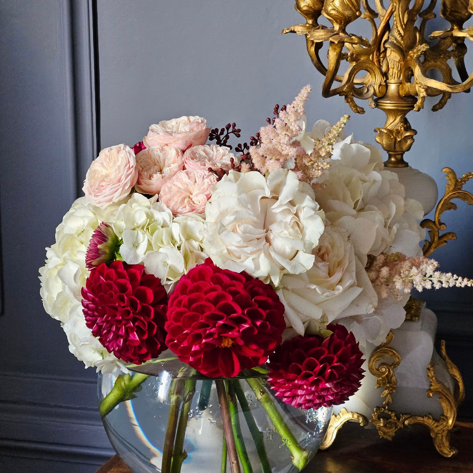 Bouquet de fleurs blanches, roses et rouges dans un vase en verre à côté d'un candélabre doré