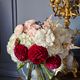 Bouquet de fleurs blanches, roses poudrés et rose foncé dans un vase en verre, à côté d'un lustre doré