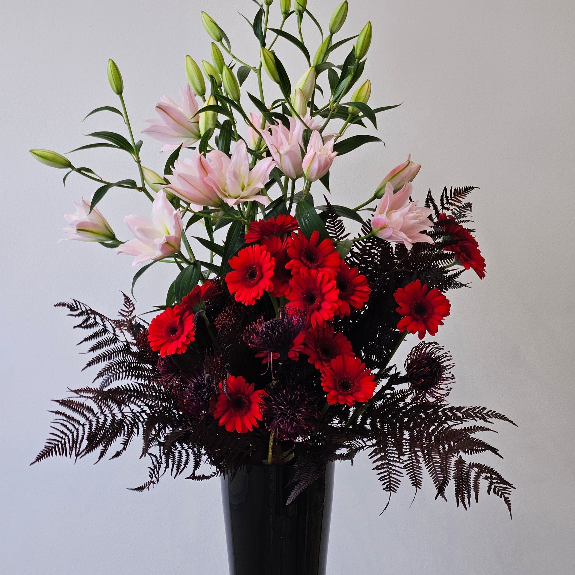 Bouquet de gerberas rouges et de lys roses au feuillage sombre dans un vase noir