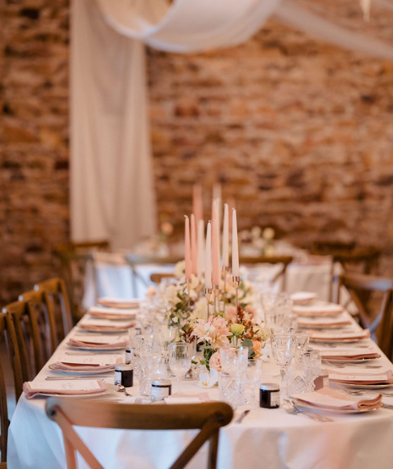 Élégante table de banquet avec nappe blanche, centre de table floral, bougies et couverts dans une salle rustique en briques