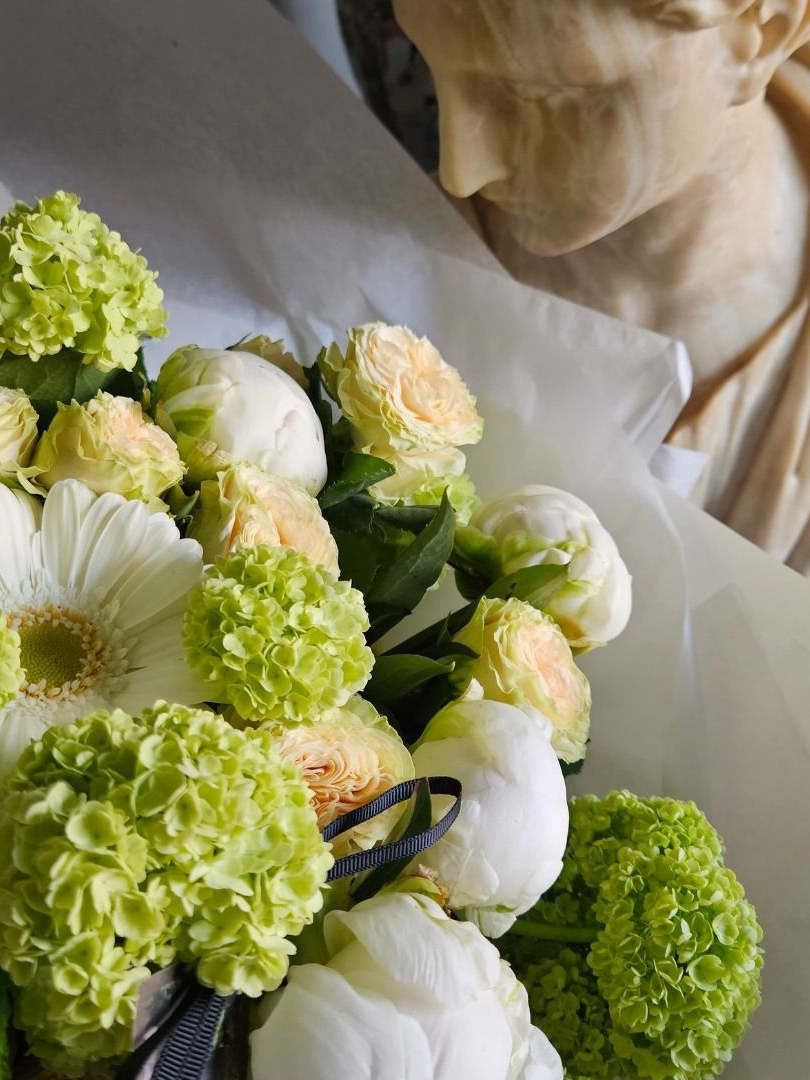 Bouquet de fleurs vert pâle et blanches à côté d'un buste en marbre sur un tissu drapé