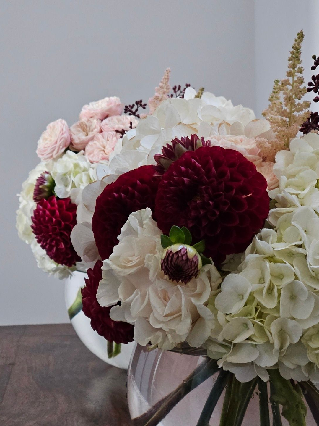 Un assortiment de fleurs roses, bordeaux et blanches disposées dans un vase en verre sur une table