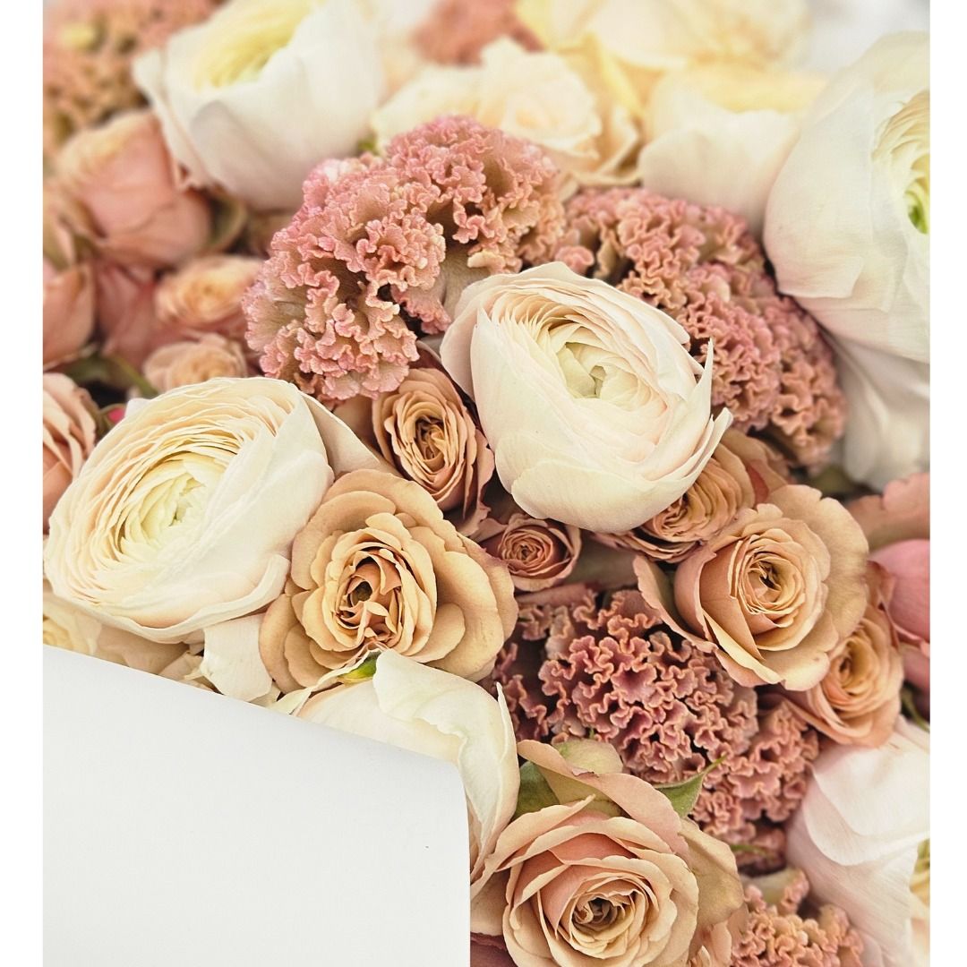 Un bouquet de roses crème et rose pâle, avec une carte blanche en bas à gauche.