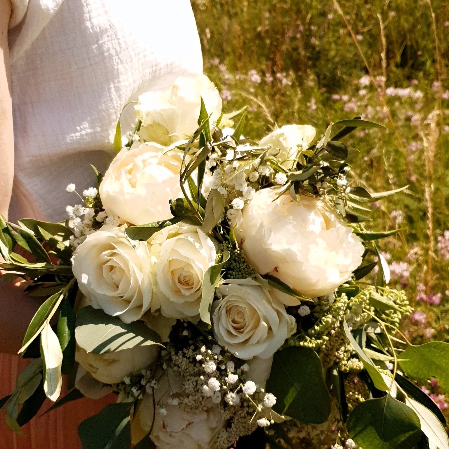 Bouquet de roses blanches et de verdure tenu à l'extérieur au soleil