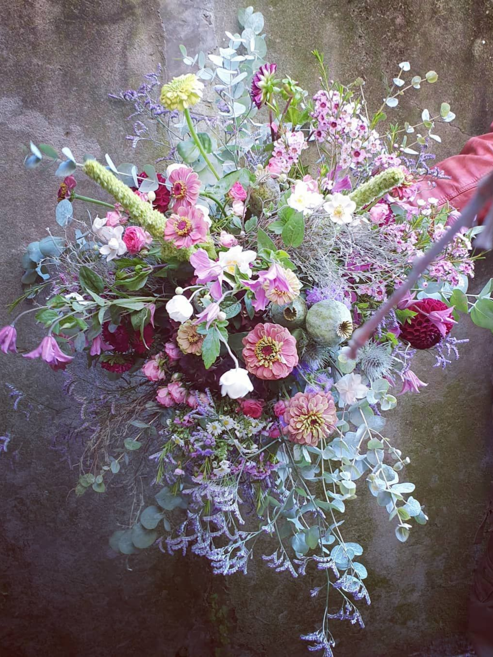 Bouquet pastel de fleurs roses, blanches, jaunes et lavande avec un feuillage bleu-vert sur un fond texturé