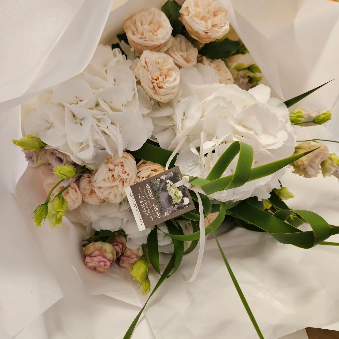 Bouquet de roses blanches et roses poudrées emballé dans du papier blanc avec des feuilles vertes et une étiquette cadeau