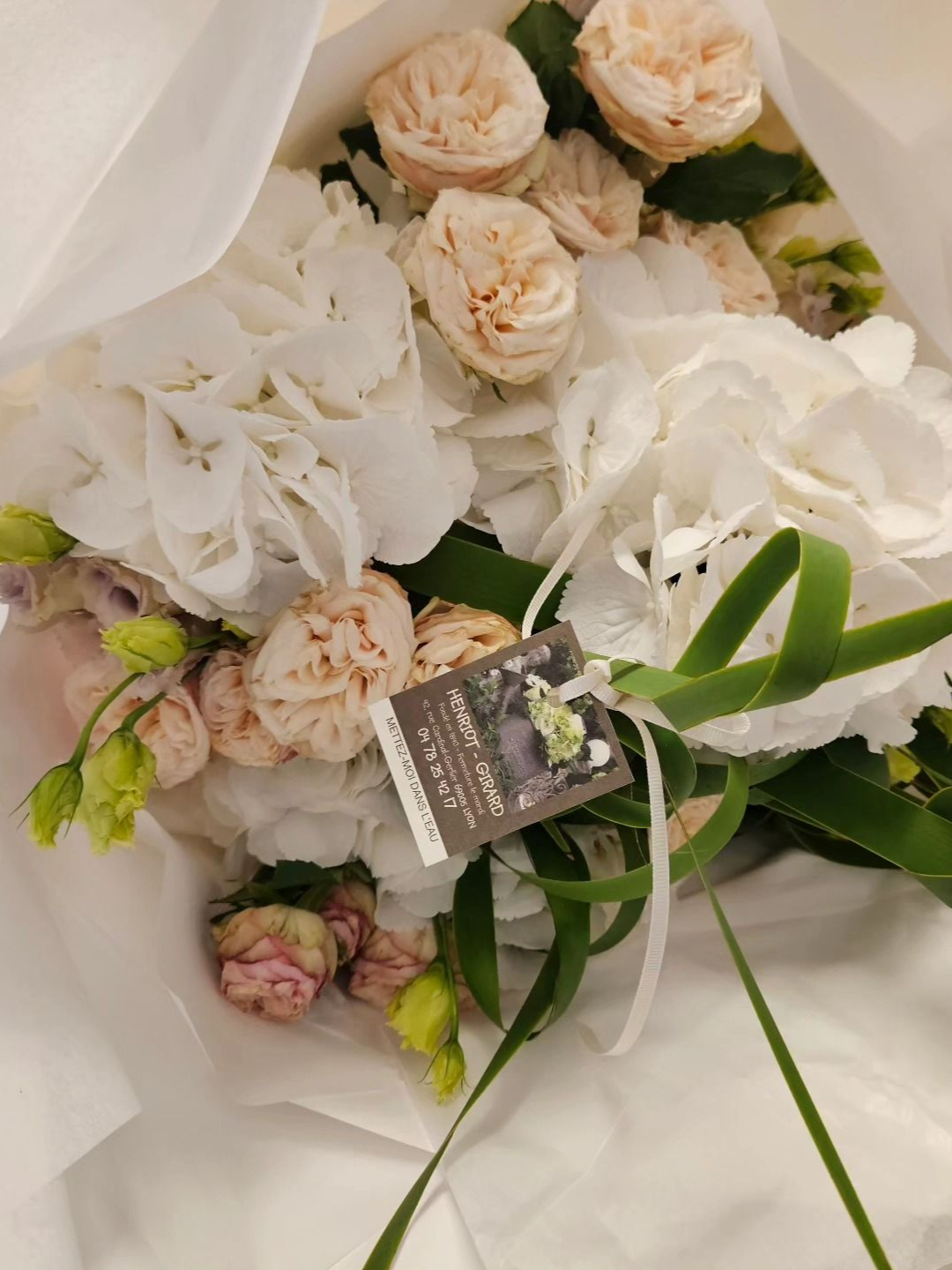 Bouquet de roses blanches et roses poudrées emballé dans du papier blanc avec des feuilles vertes et une étiquette cadeau