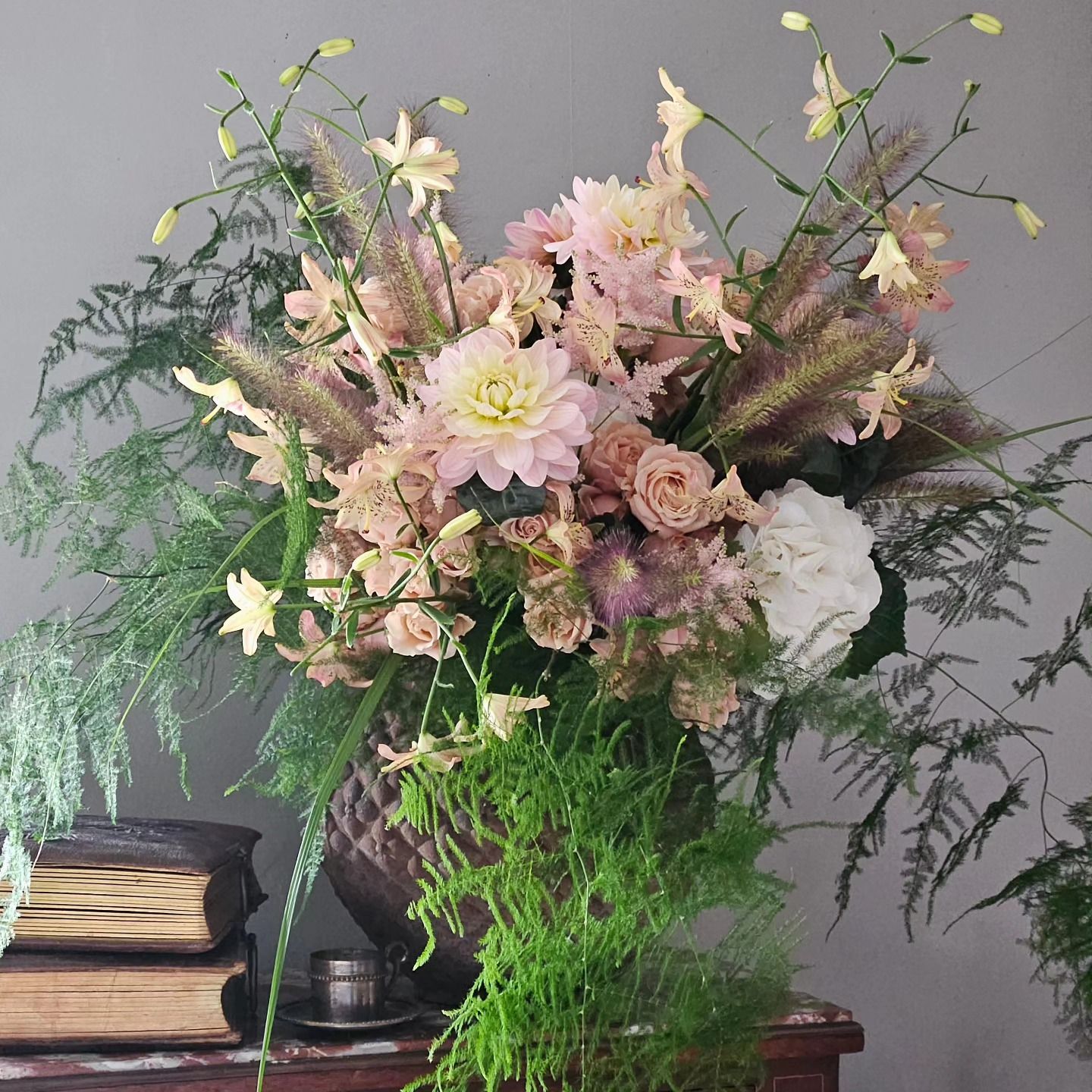 Bouquet de fleurs pastel dans un vase sur une table à côté de livres empilés, sur fond gris