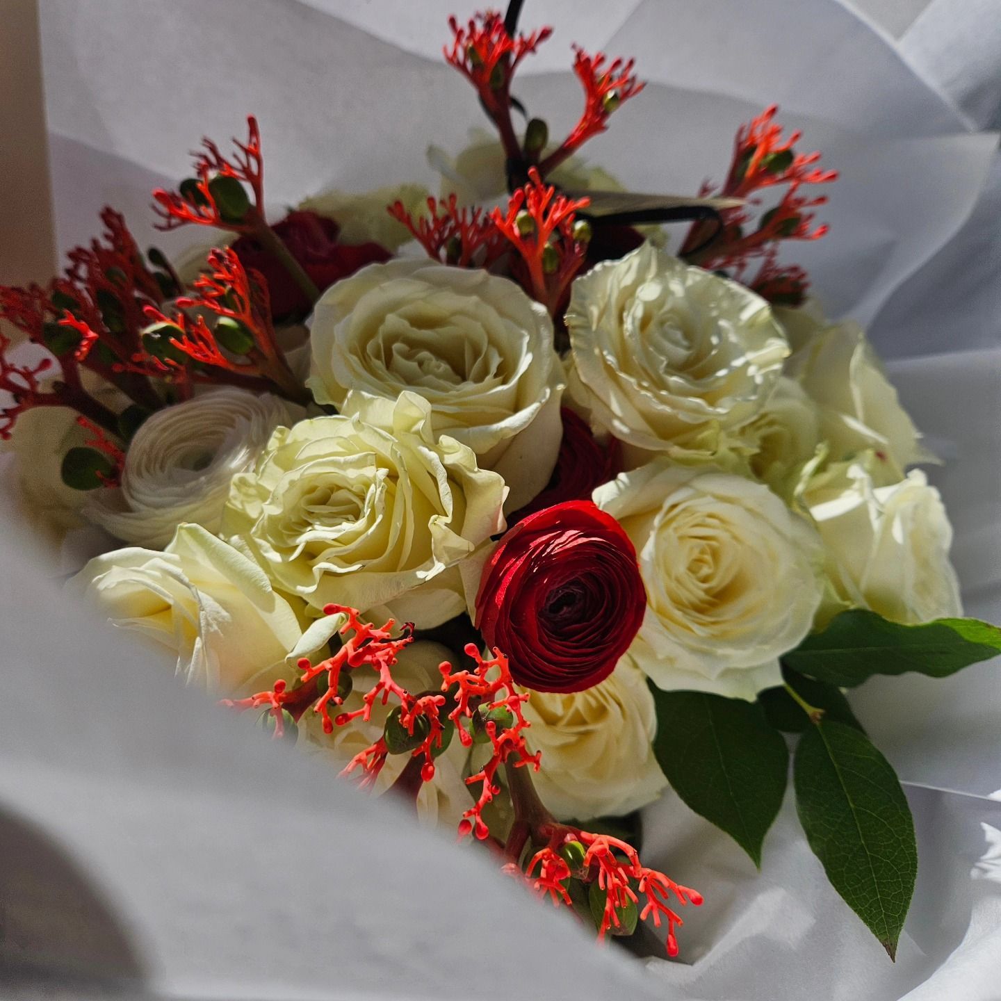 Bouquet de roses crème et rouges avec des fleurs rouges d'accompagnement, emballé dans du papier blanc