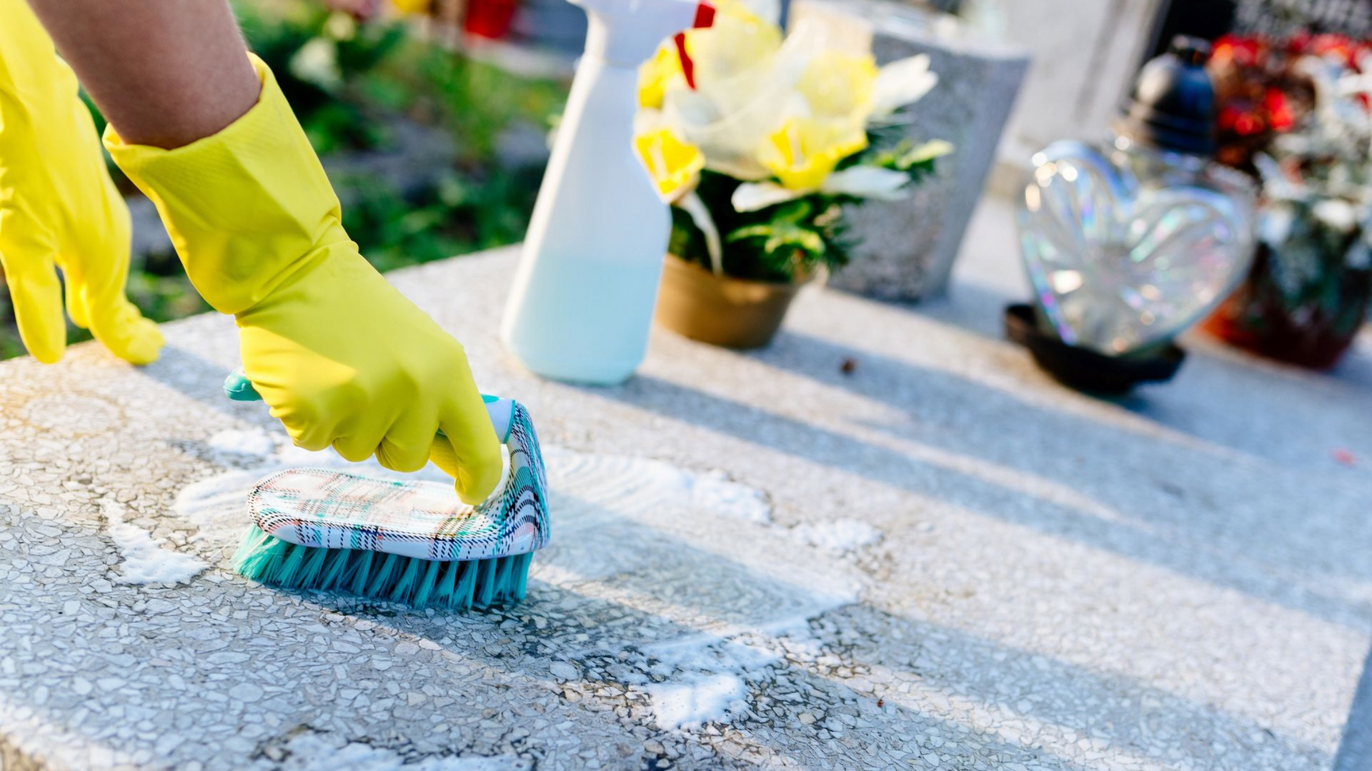 Des mains gantées de jaune frottent une surface de pierre fissurée à l'aide d'une brosse, à l'extérieur.