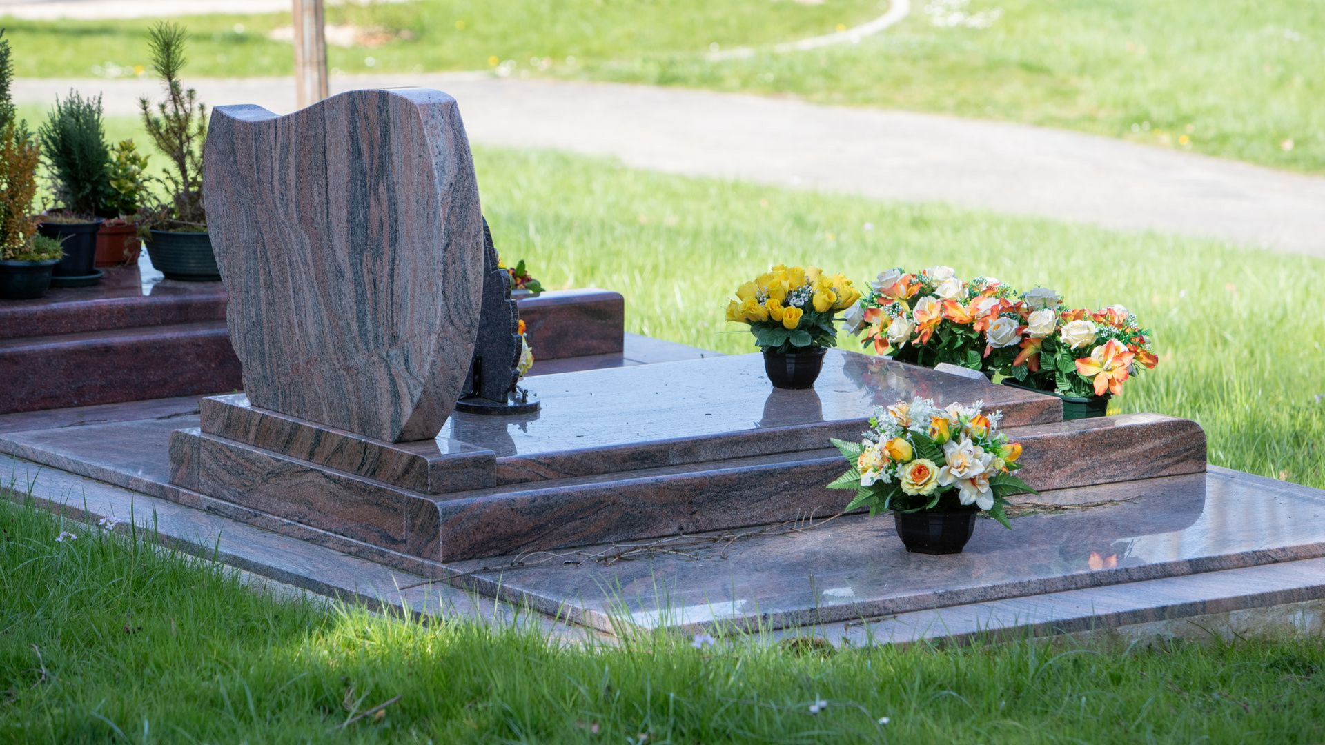 Monument funéraire orné de compositions florales dans un cimetière, installé sur une pelouse.