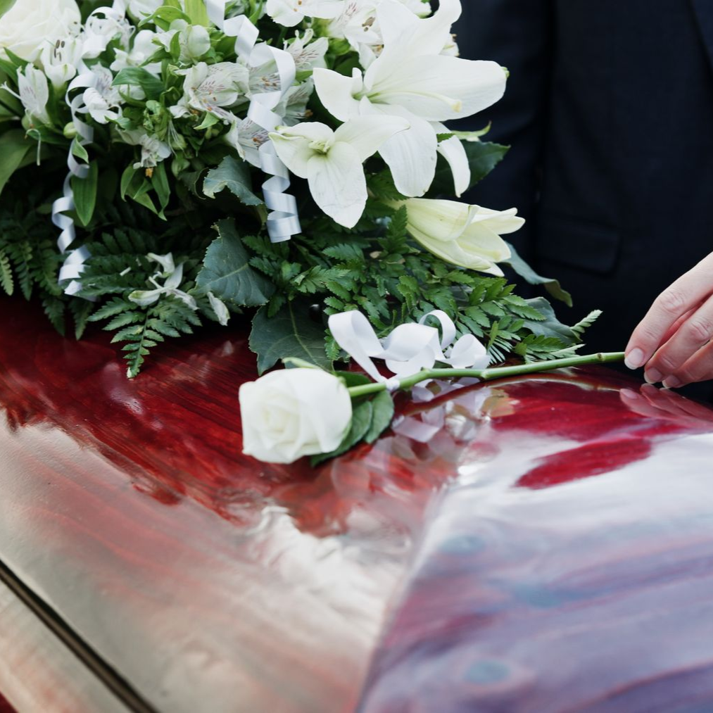 Des fleurs blanches et une rose solitaire sur un coffret rouge poli, une main arrangeant la tige