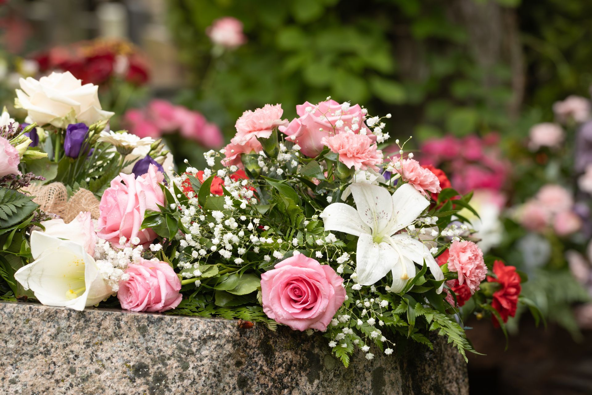 Des bouquets de fleurs roses, blanches et violettes disposés sur un rebord de pierre à l'extérieur