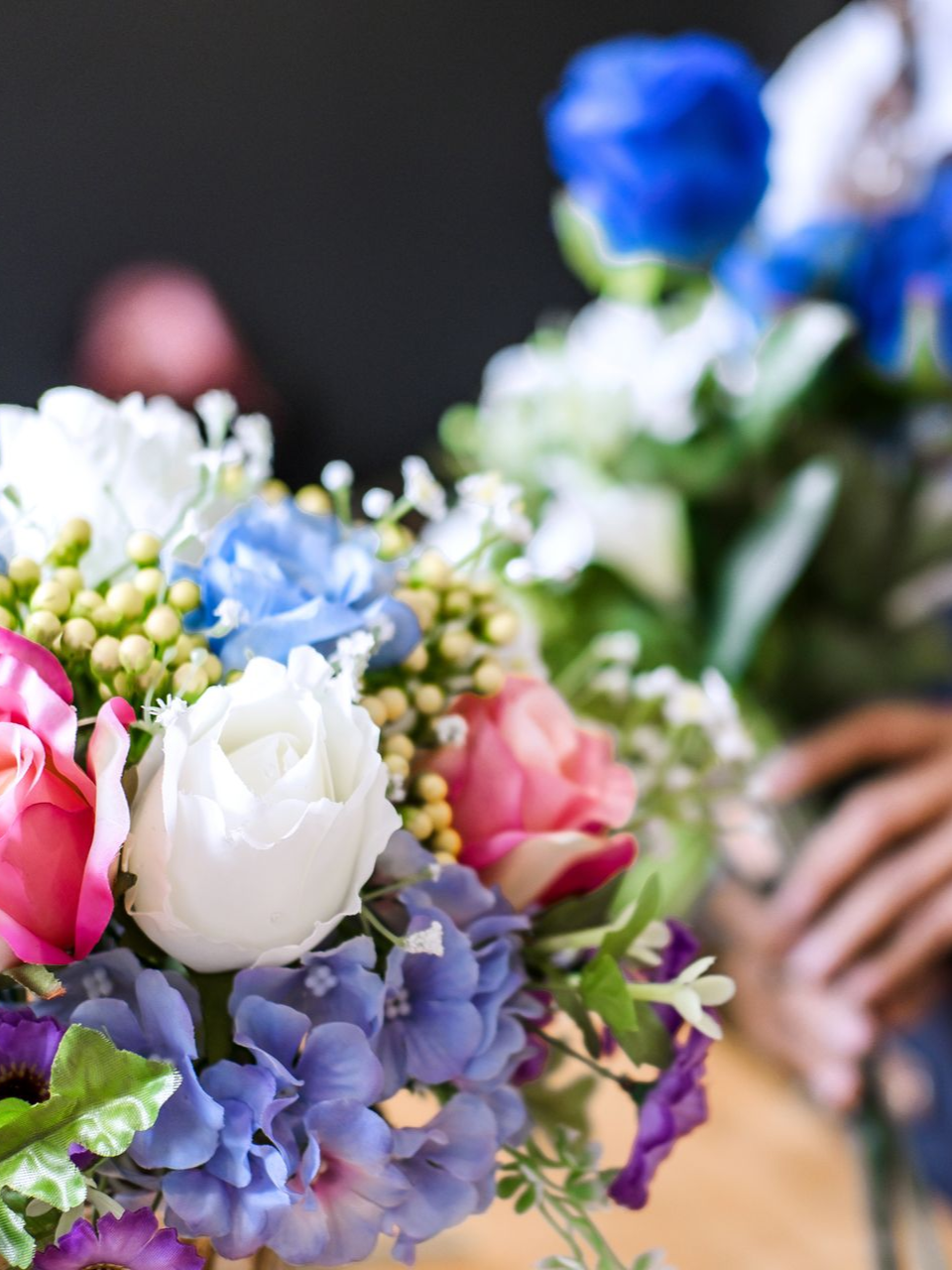 Un bouquet coloré de fleurs blanches, roses, bleues et violettes tenu dans une main