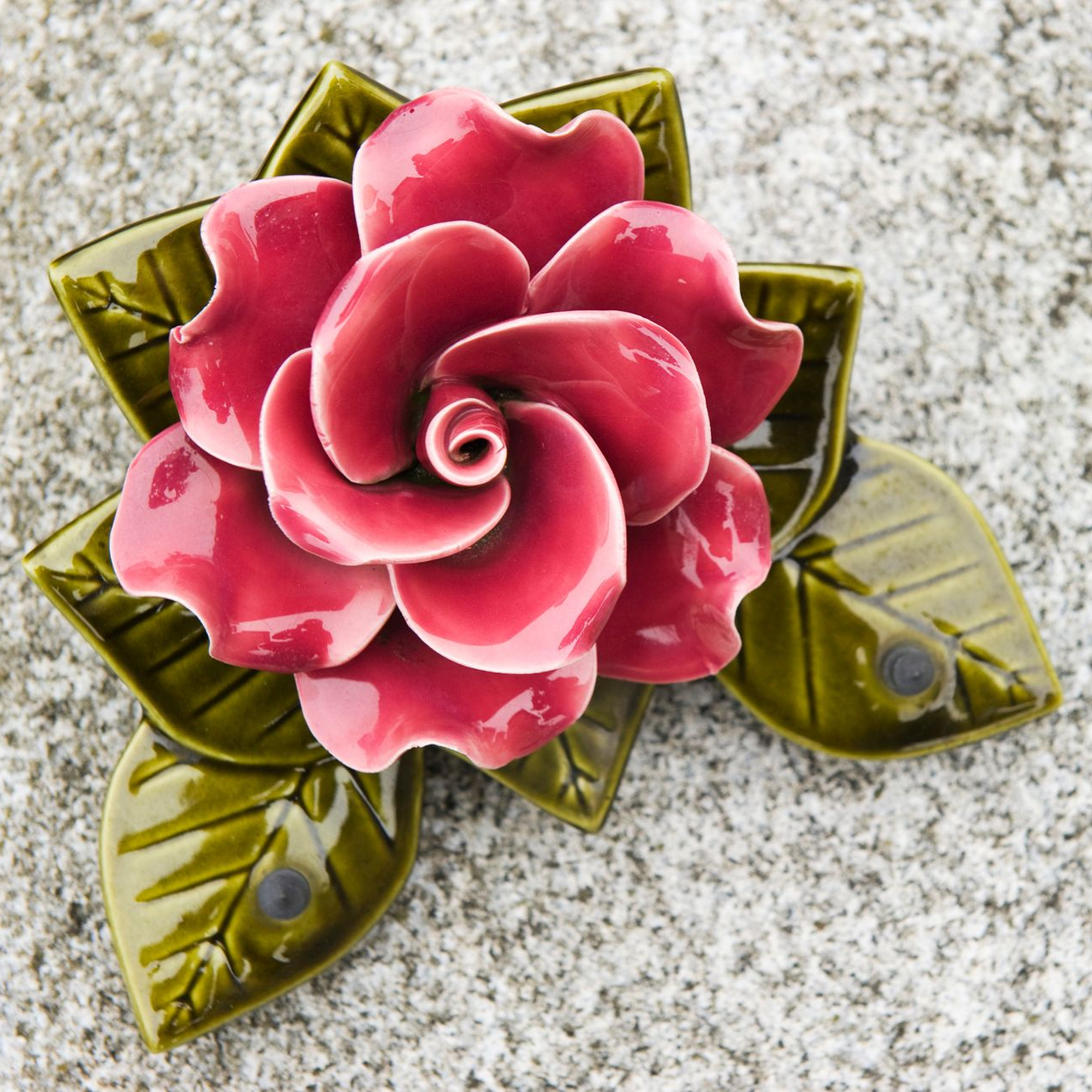 Broche en forme de rose rose avec des feuilles vertes sur une surface grise mouchetée