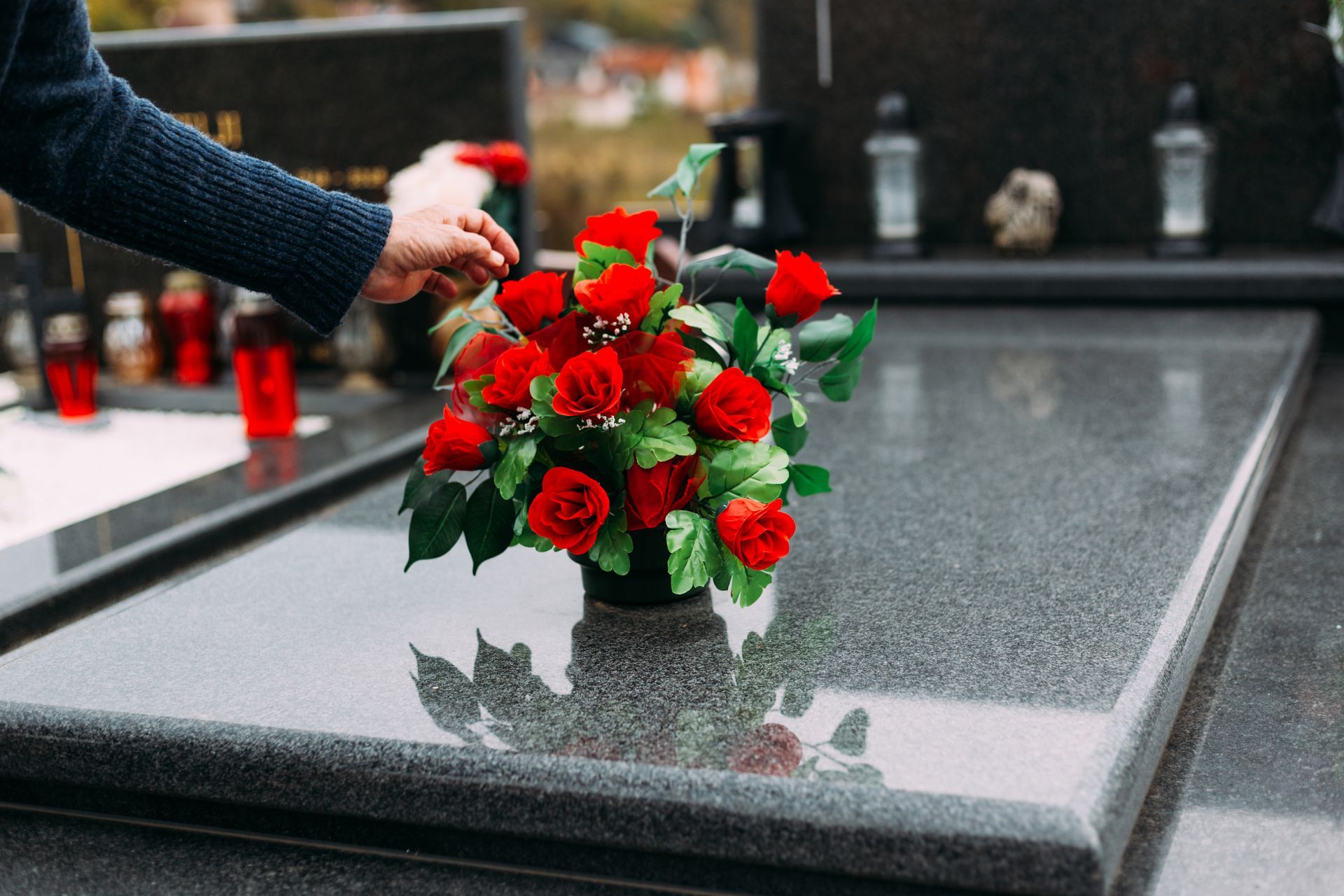 Une main déposant un bouquet de fleurs rouges et blanches sur une pierre tombale polie