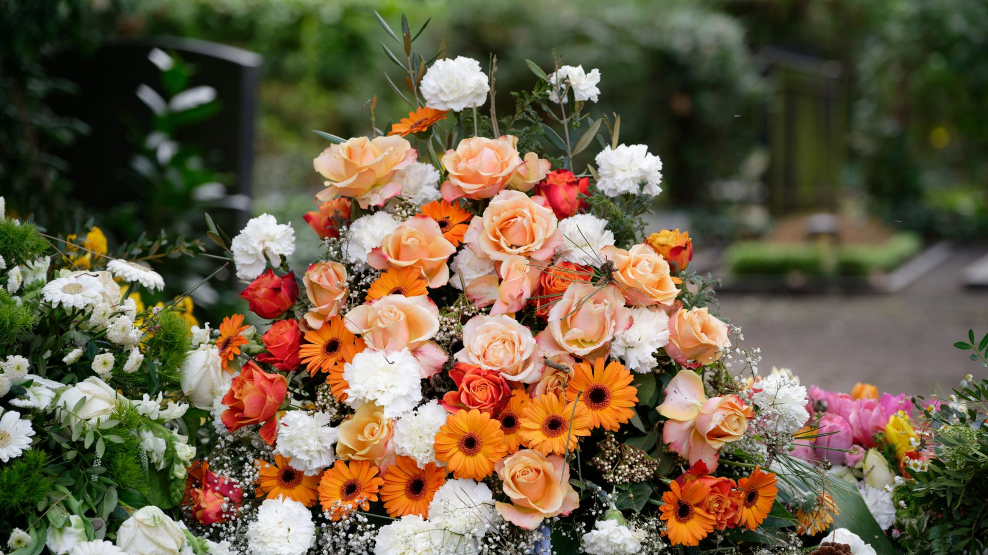 Un grand bouquet de fleurs orange, pêche et blanches disposé à l'extérieur, dans un jardin.