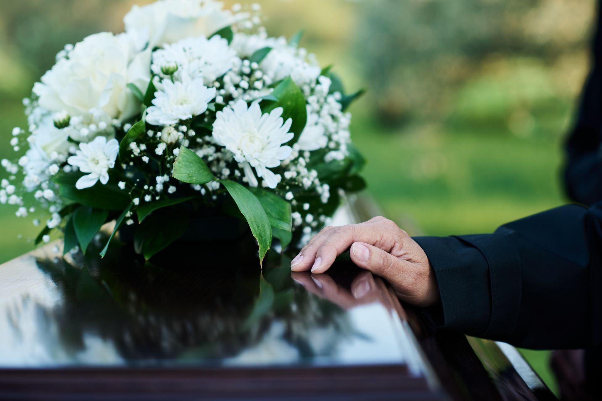 Des fleurs blanches près d'une main posée sur un cercueil poli lors de funérailles en plein air